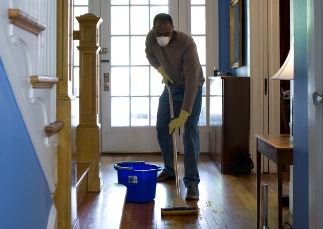 Homem limpando chão de casa usando máscara