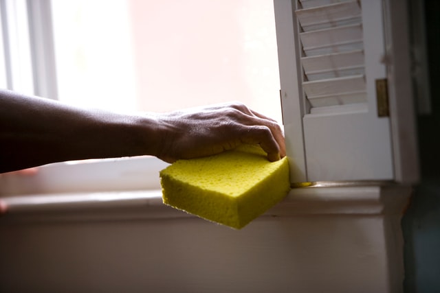 Mão com bucha amarela limpando a janela