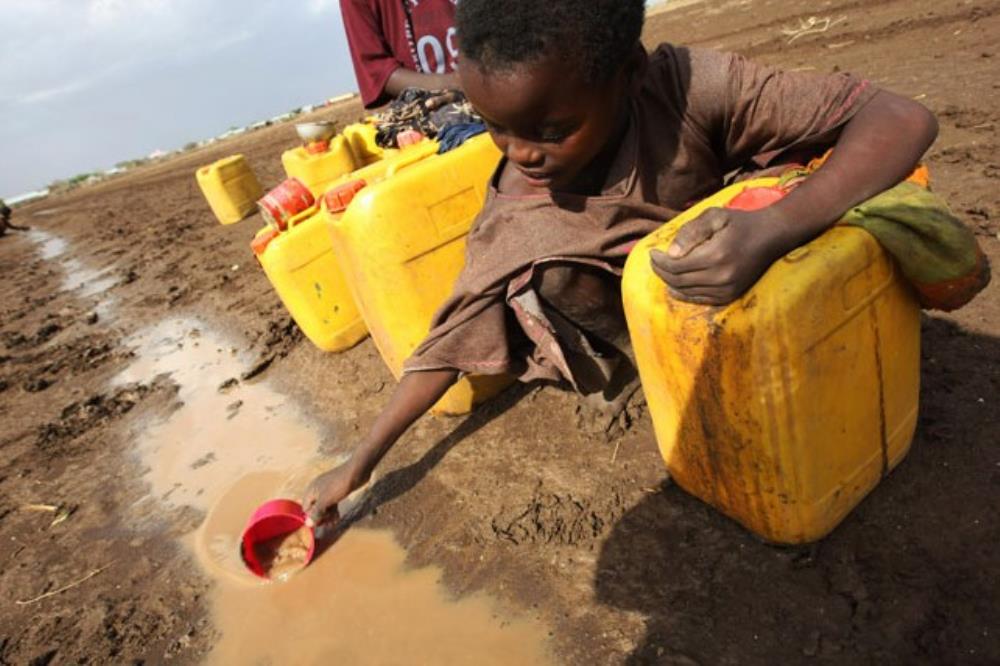 Criança em região com falta de acesso a água potável colhe água da rua para engarrafar.