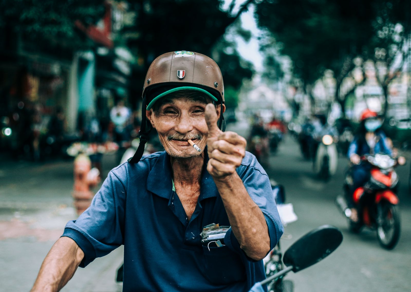 Idoso branco numa motocicleta, sorrindo com o polegar levantado.