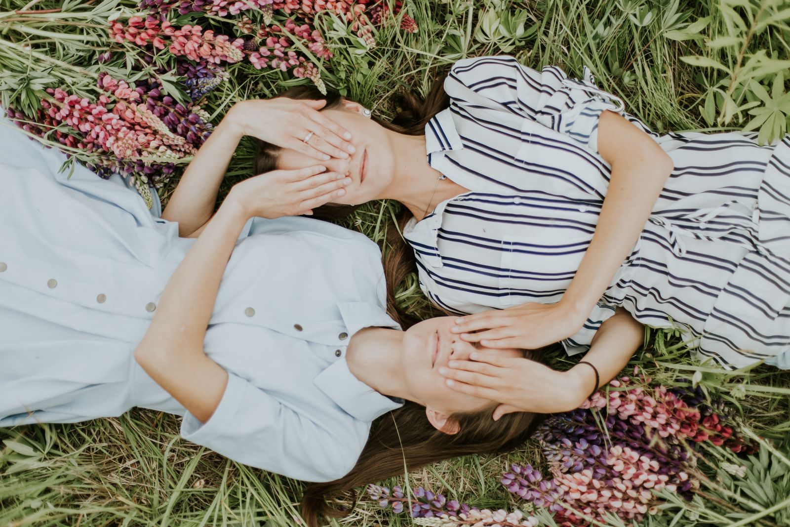 Duas meninas gêmeas deitadas na grama, cobrindo os olhos uma da outra.