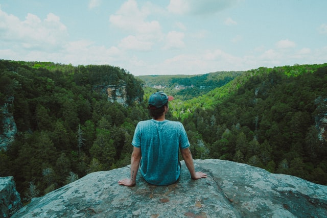 Homem sentado numa pedra observando a paisagem.