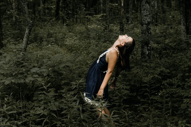 Mulher branca usando vestido azul marinho numa floresta.