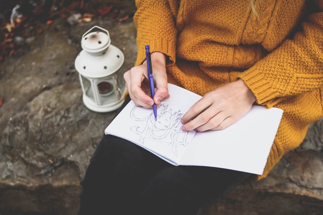 Mulher branca desenhando num caderno.