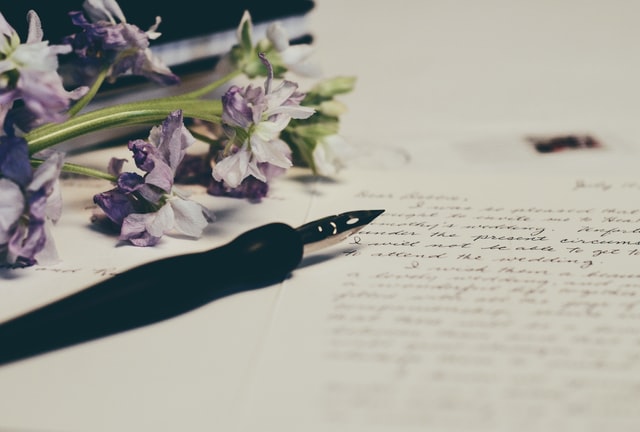 Caneta e flores roxas em cima de papel de carta.
