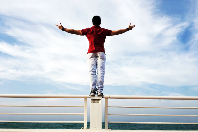 Sanketh Rao de Pexels Homem com os braços abertos em cima de um patamar, indicando independência