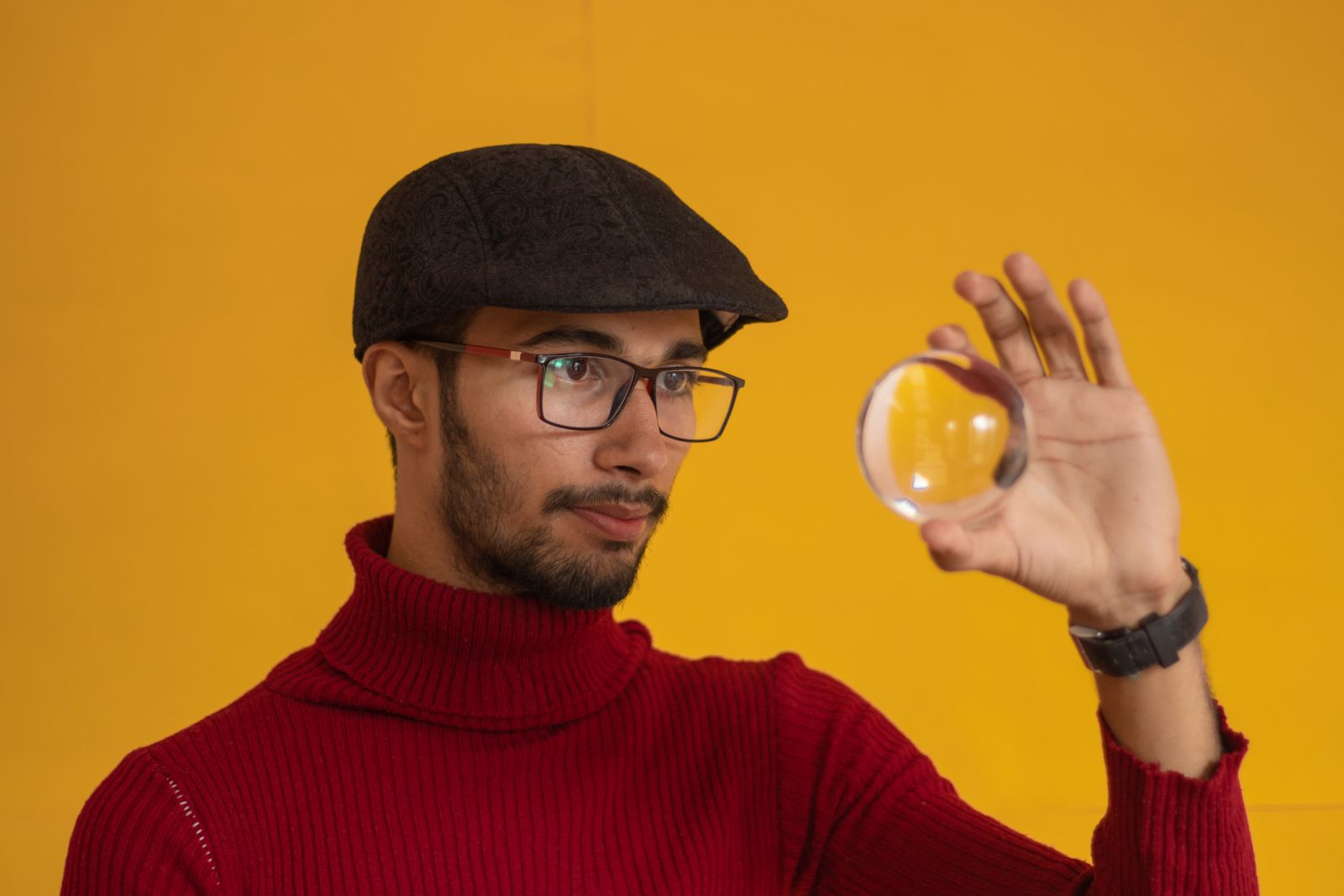 Homem usando uma boina e uma blusa de frio olhando para uma bola de vidro.