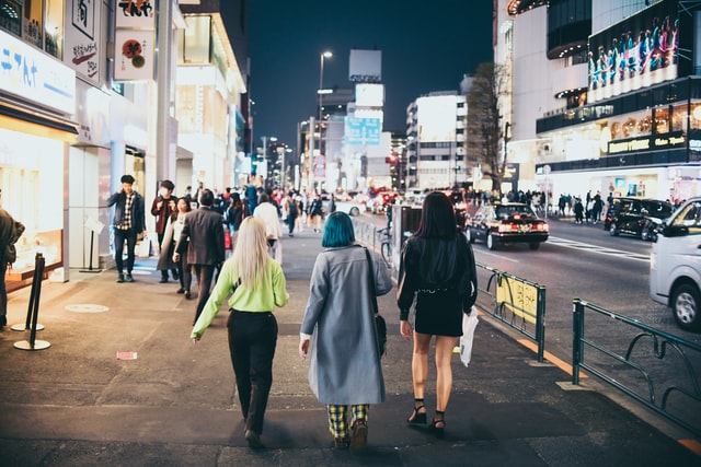Mulheres andando numa avenida movimentada a noite.
