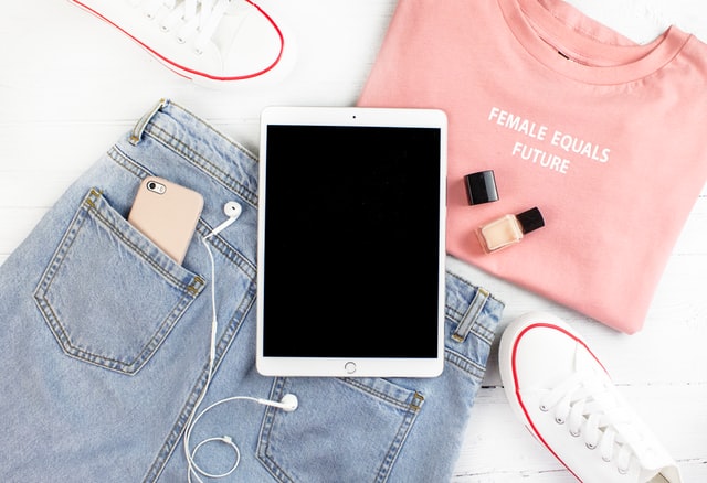 Camiseta rosa, short jeans azul e tablet em cima de bancada branca.