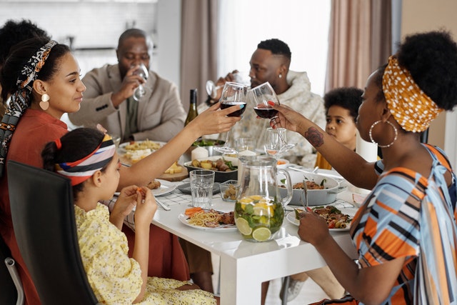 Família reunida a uma mesa para o almoço, brindando com taças de vinho.