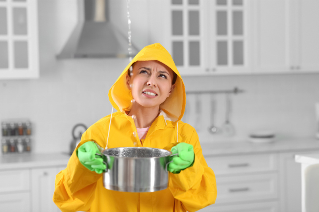 Mulher com capa de chuva com um balde para goteira dentro de casa