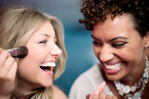 Duas mulheres dando risada enquanto se maquiam 