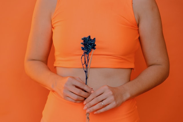 Mulher usando roupas laranjas, segurando flores azuis.