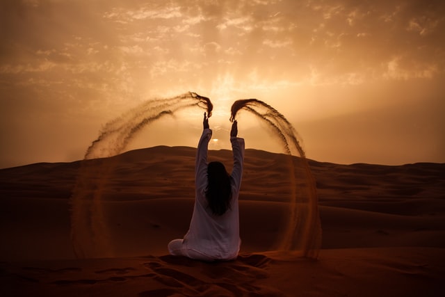 Silhueta de mulher sentada de costas num deserto, jogando areia para cima.