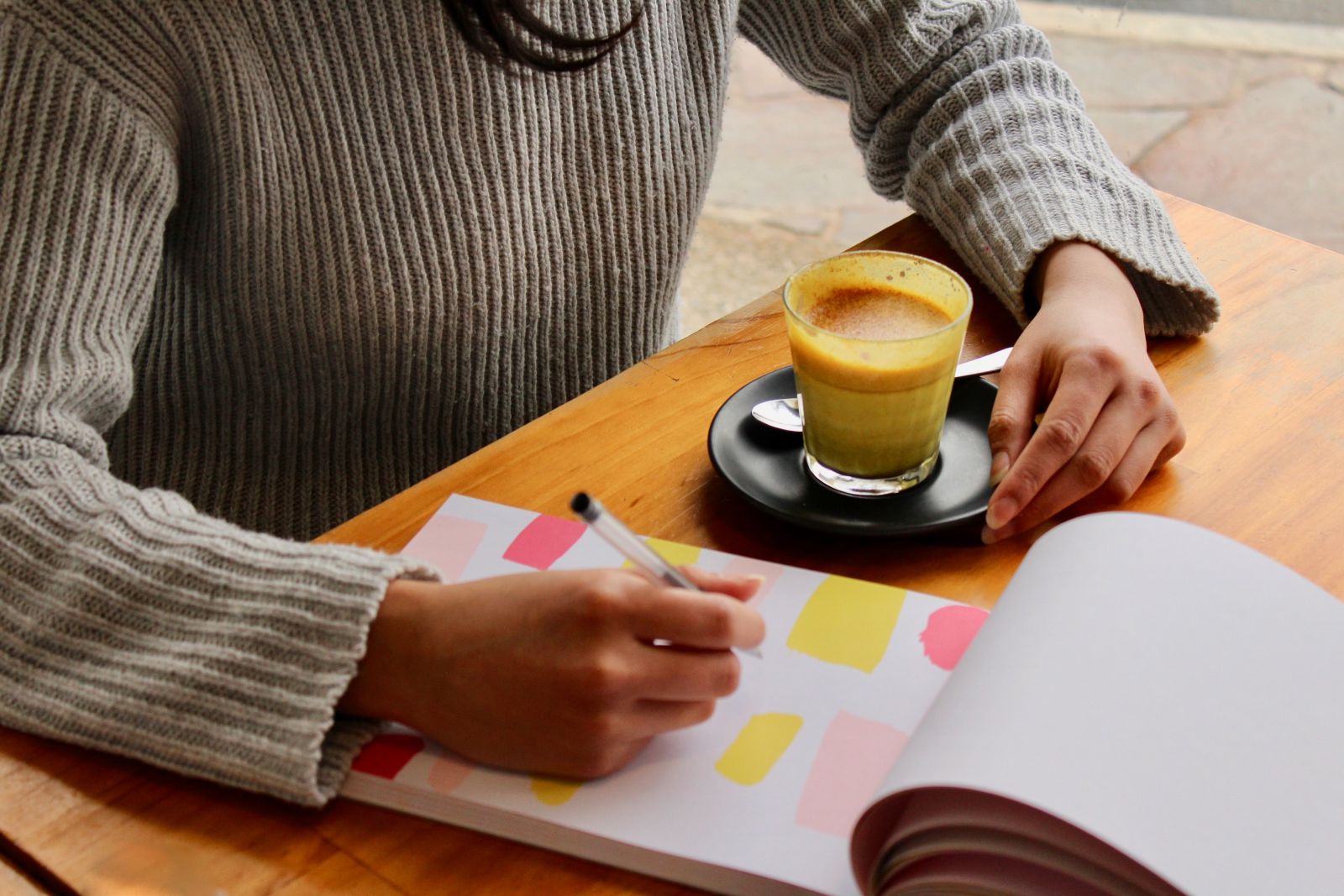 Mulher desenhando em seu caderno ao lado de uma xícara de café