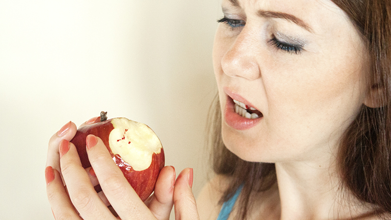 Menina com o dente e a gengiva sangrando após comer uma maçã
