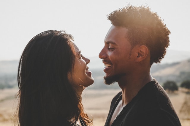 Homem negro e mulher asiática sorrindo e se olhando.