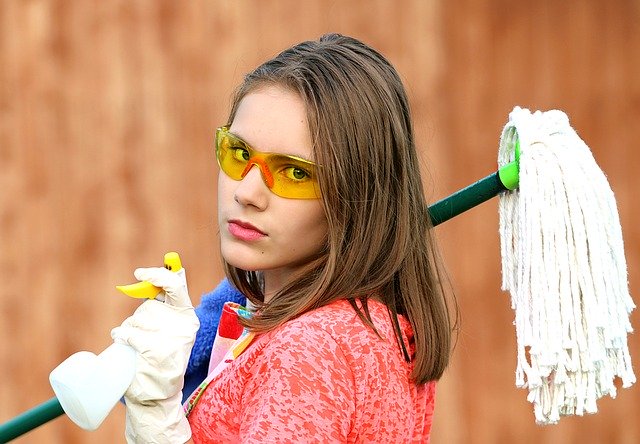 Mulher com óculos de proteção segurando rodo e produtos de limpeza