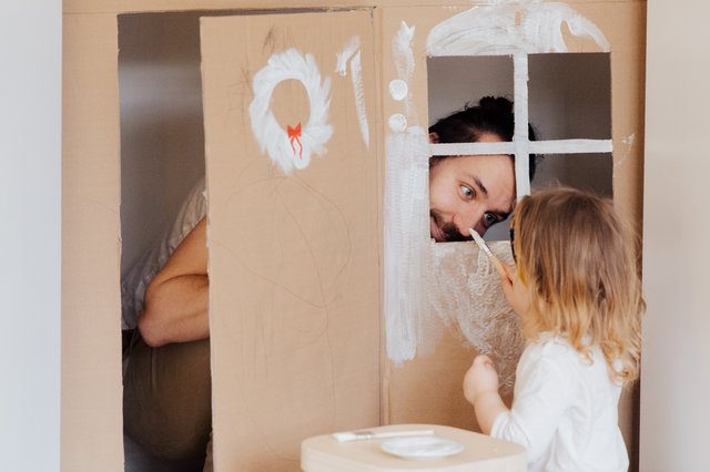 Pai brincando com sua filha em uma casinha de papelão.