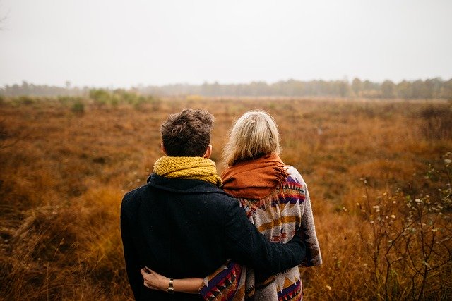 Homem e mulher abraçados vistos de costas em um campo.