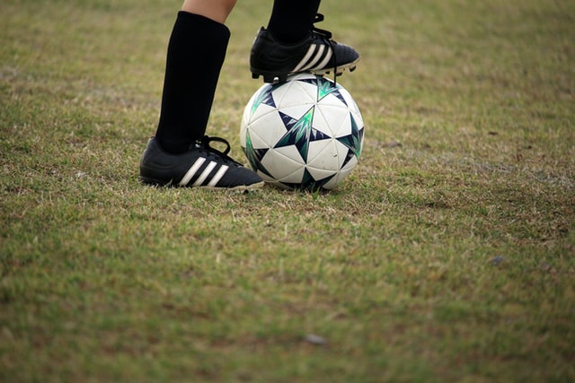 Par de pés posicionados perto de uma bola de futebol 
