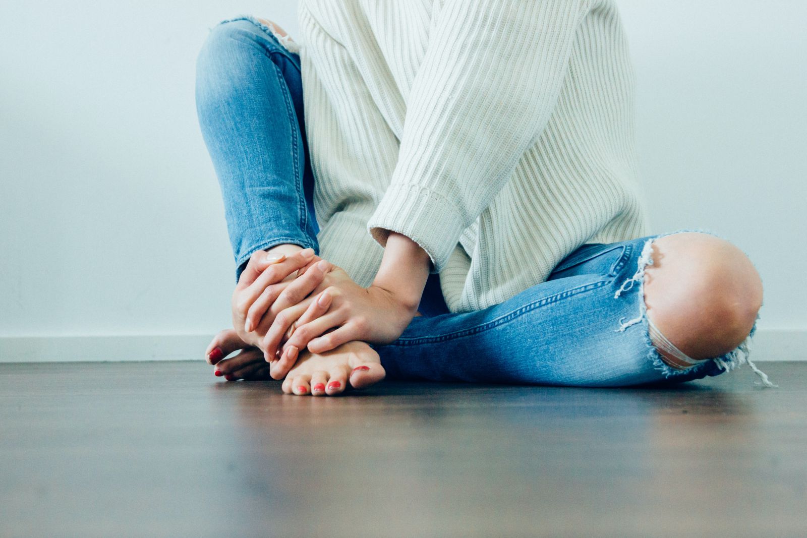 Mulher sentada no chão segurando seu pé com suas mãos