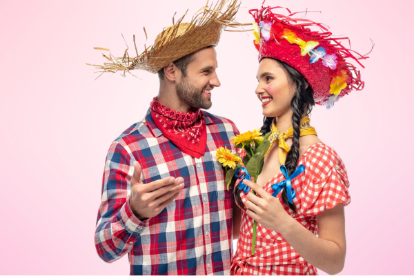 Homem e mulher ocm trajes típicos de festa junina, sorrindo e se olhando.