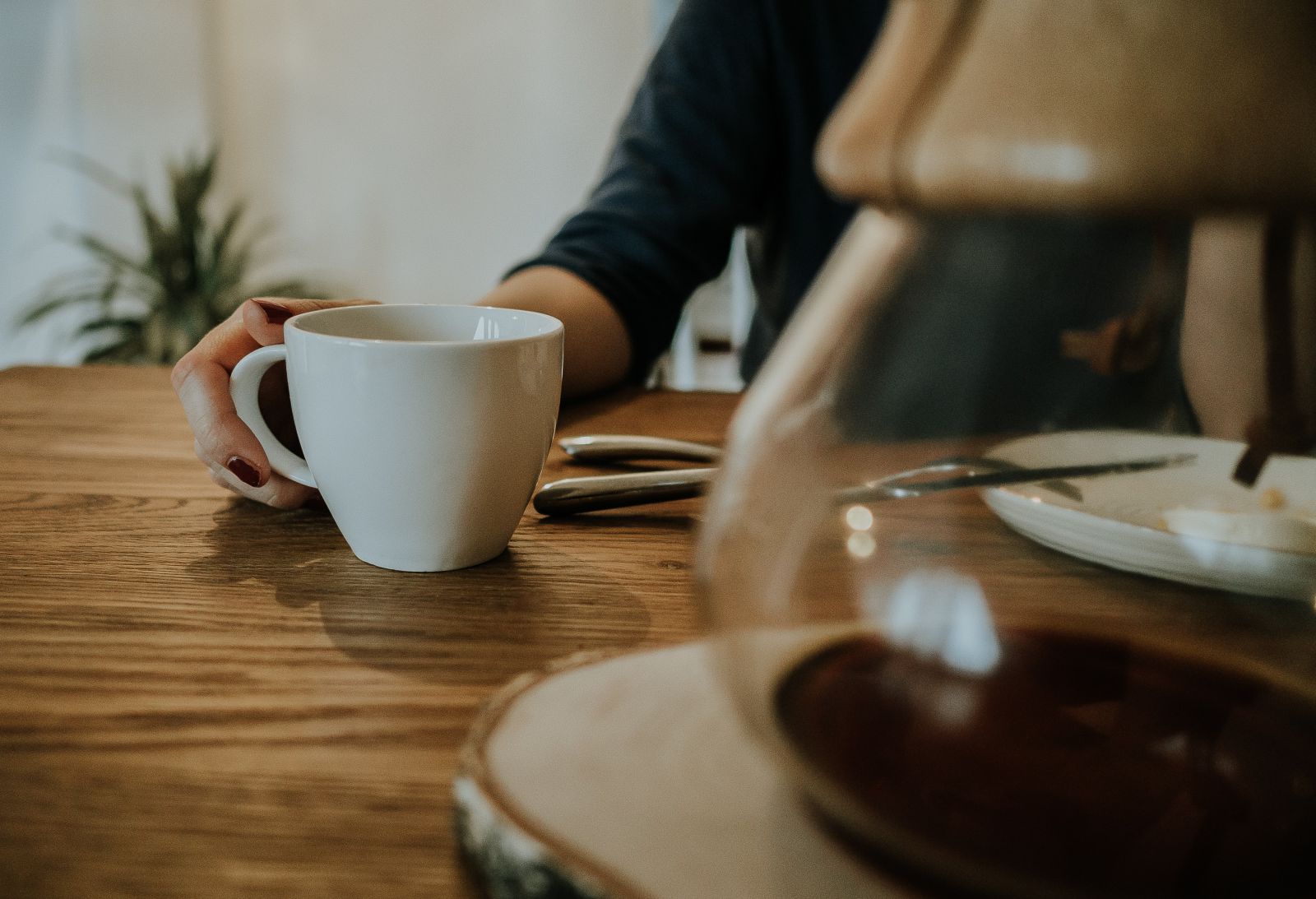 Mulher sentada ao lado de uma cafeteira e uma xícara de café