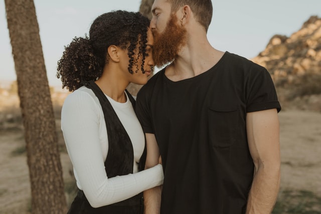 Homem branco beijando testa de mulher negra.