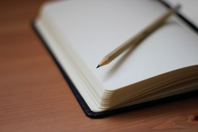 Caderno aberto sobre uma mesa de madeira, junto a um lápis.