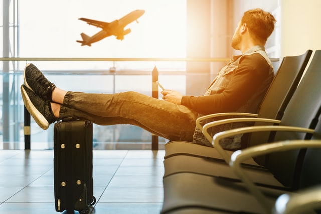 Homem branco sentado em cadeira num aeroporto.