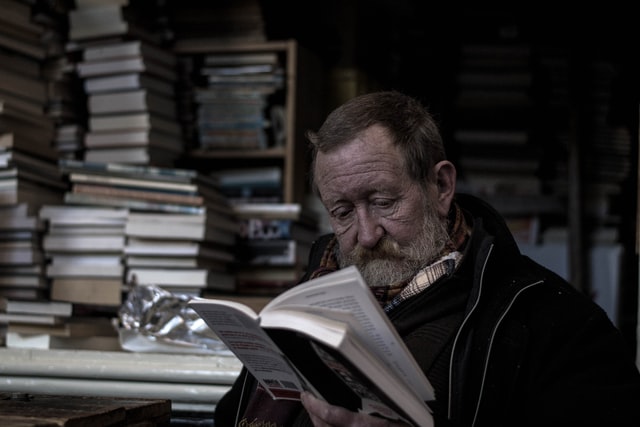 Homem idoso branco lendo livro.