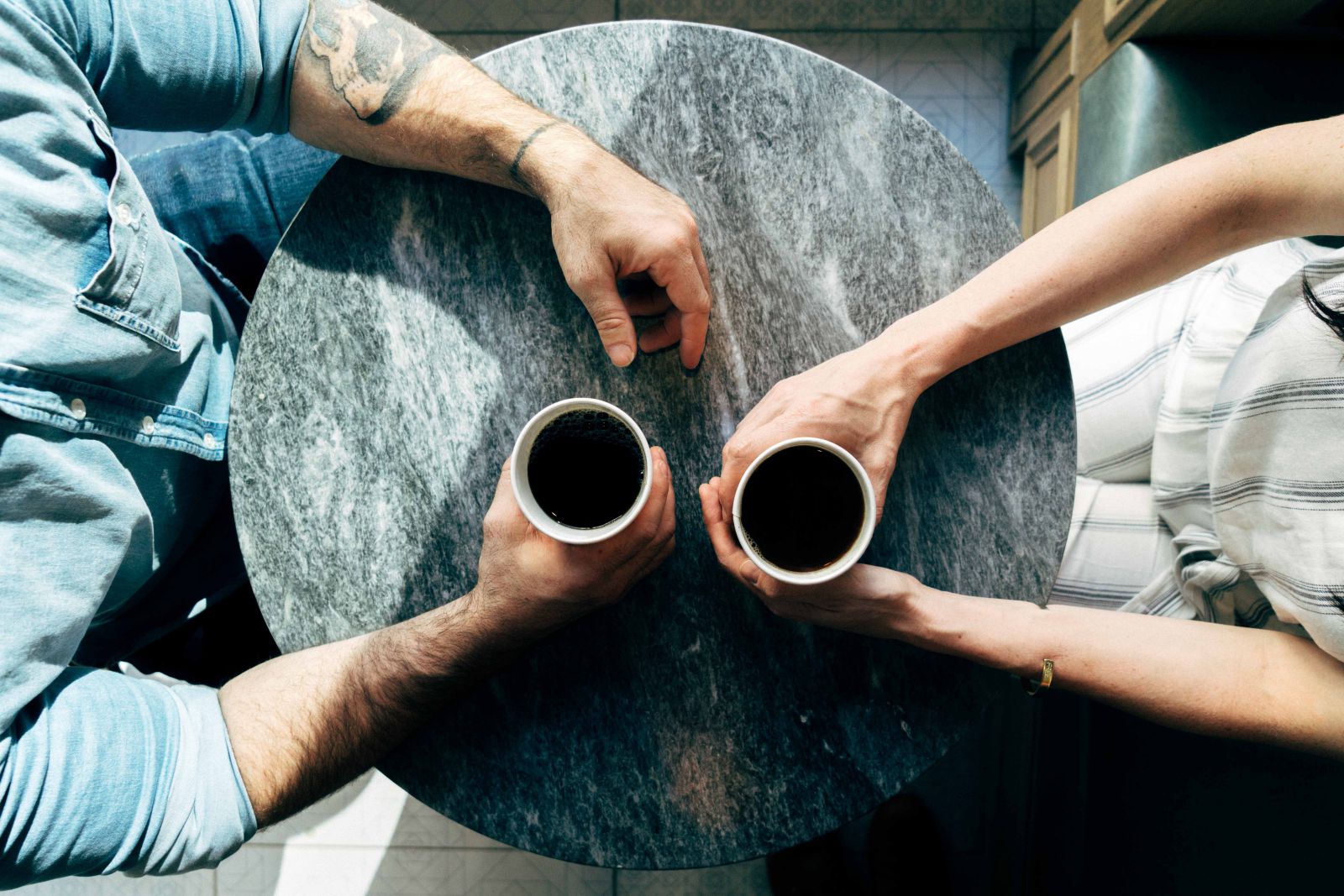 Homem e mulher sentados em uma mesa segurando copos de café