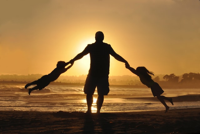 Pai girando seus dois filhos no ar com as mãos, na praia