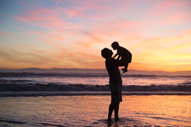 Pai com seu filho no colo, na praia, ao pôr do sol