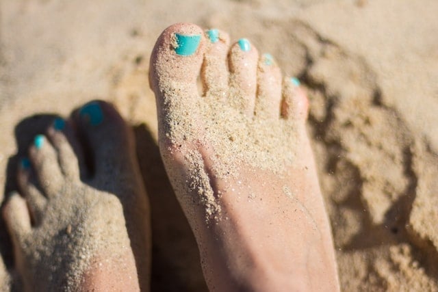 Unhas azuis em pé cheio de areia.
