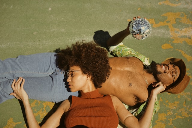 Homem negro deitado na areia, e mulher negra com a cabeça deitada na barriga dele.