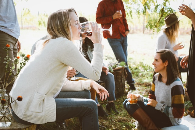 Mulher branca bebendo vinhos com amigos.
