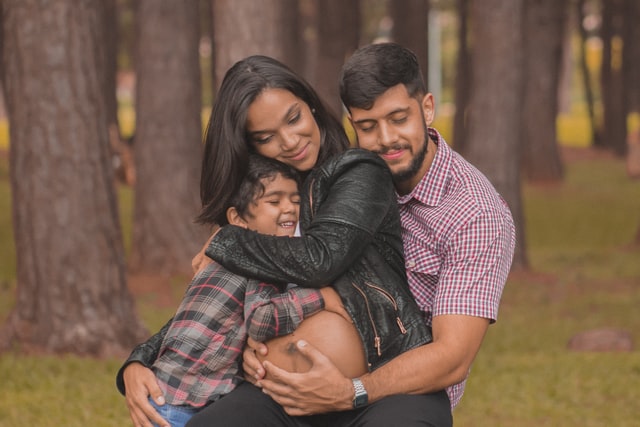 Mulher negra grávida abraçando criança e homem.