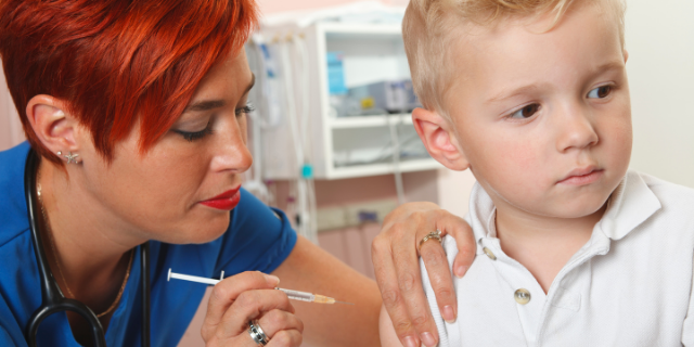 Enfermeira injeta substância em braço de menino por meio de agulha.
