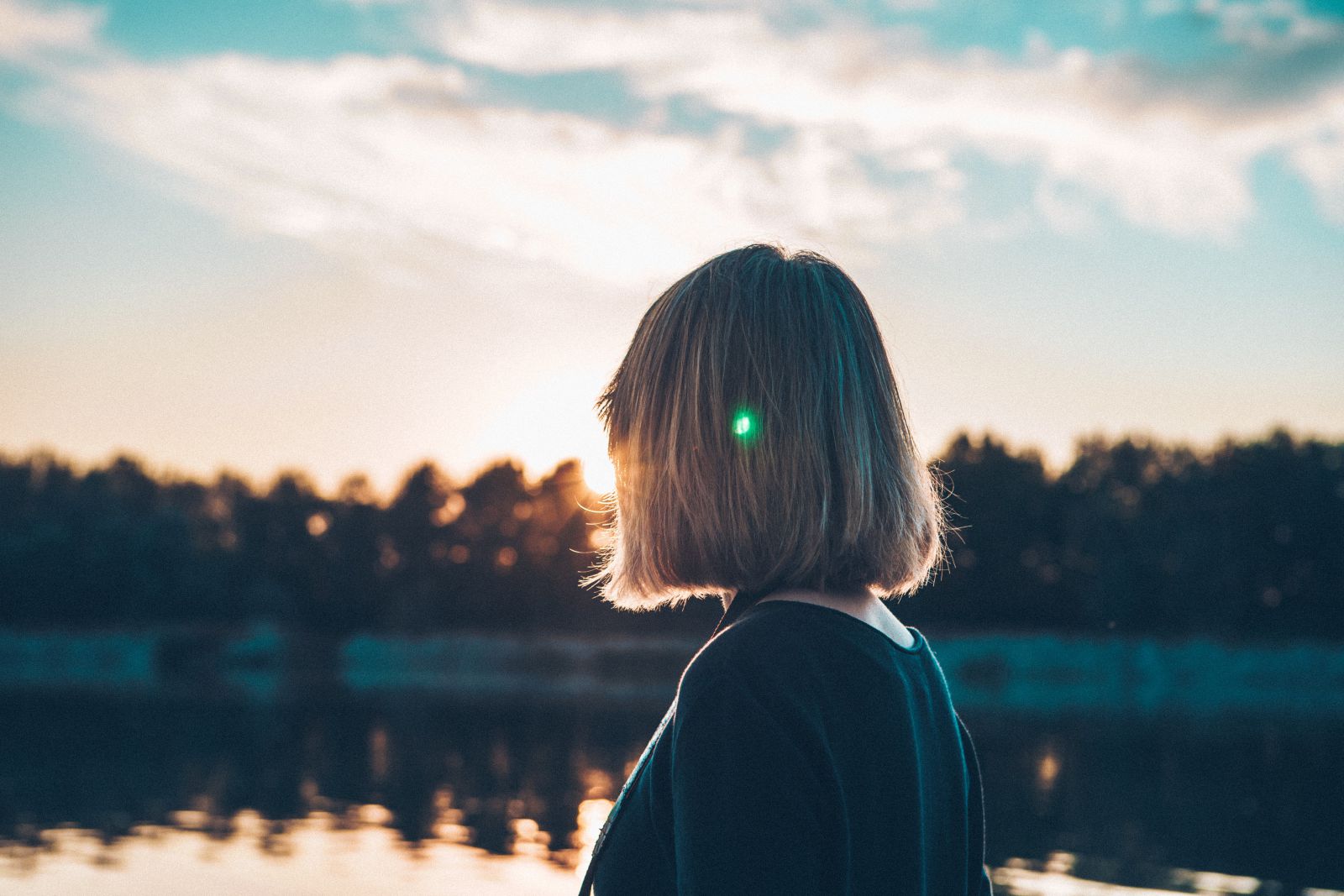 Mulher em frente a um lago  olhando para o sol 