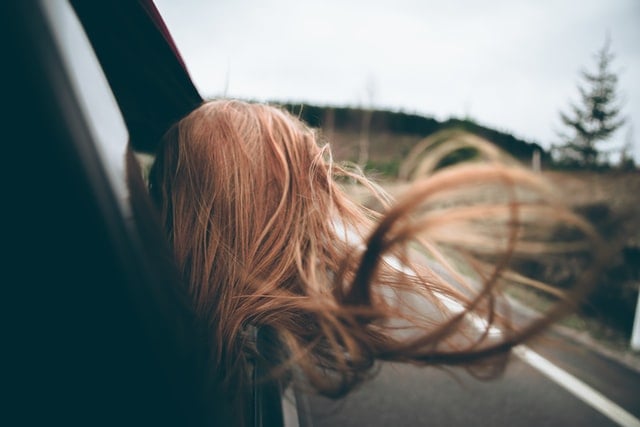 Mulher de cabelos ruivos com a cabeça para fora do carro.