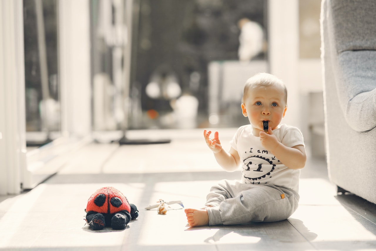 Bebê sentado no chão com alguns brinquedos em sua frente, enquanto ele segura um apito em sua boca e o assopra.