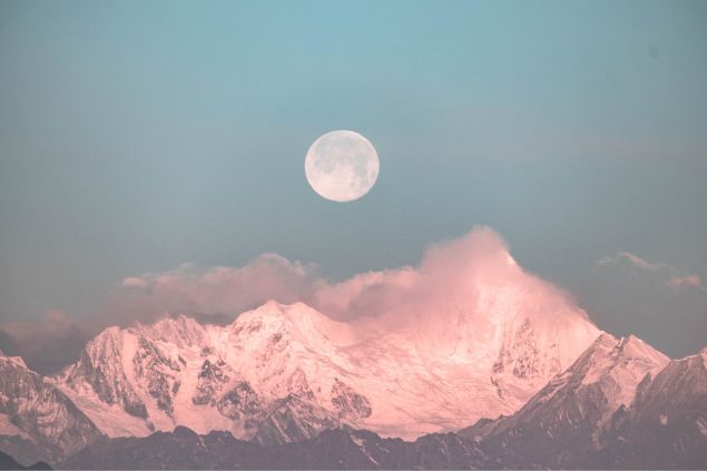 Lua cheia em um céu claro, sobre montanhas.