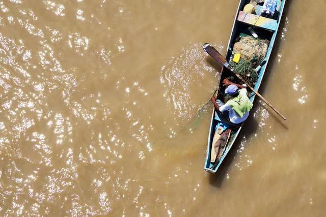Homem dentro de canoa azul num rio de água suja.