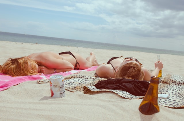 Duas mulheres brancas deitada na areia da praia.