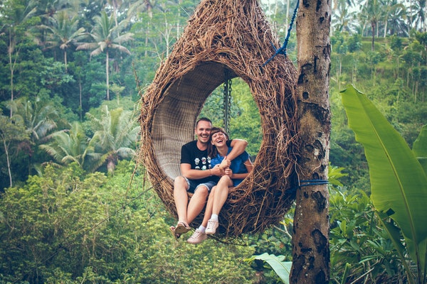 Casal sentado em balanço em formato de gota de madeira