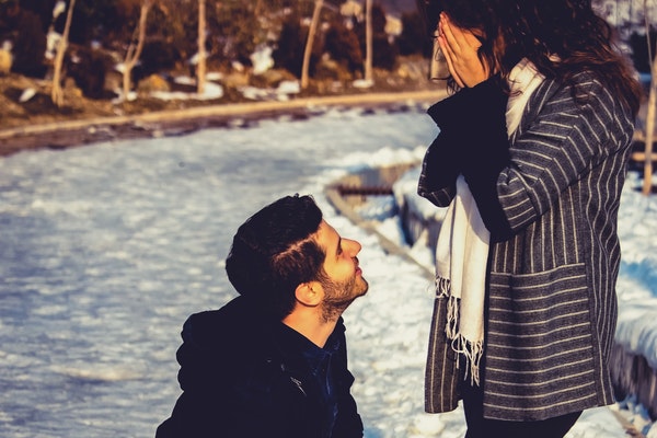 Casal na neve com namorado ajoelhado olhando para namorada
