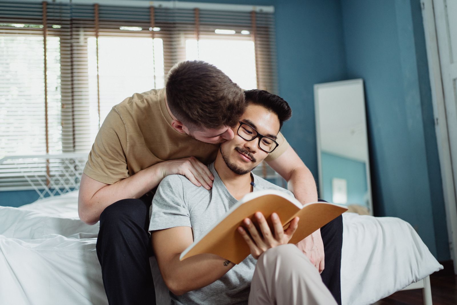 Homem lendo um livro enquanto seu namorado o beija na bochecha.