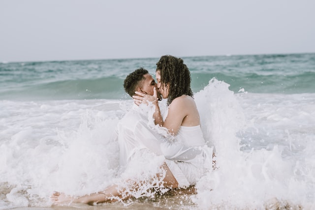 Homem e mulher se beijado em meio a ondas do mar.